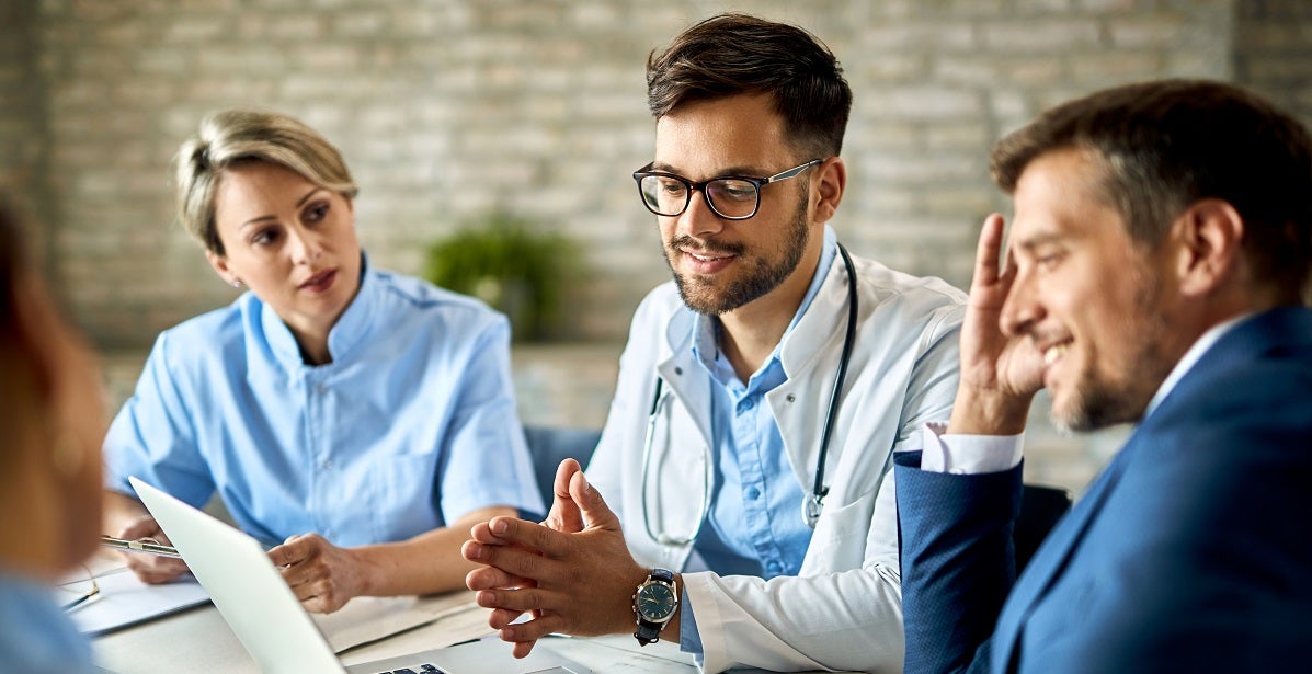 Nurse manager and other healthcare workers and businessman using laptop while having a meeting in the office