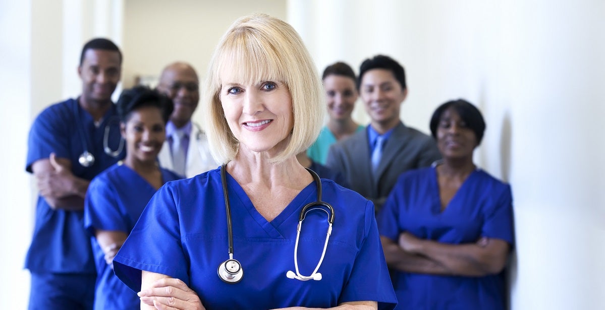Portrait smiling Caucasian female nurse with dedicated multi ethnic clinical nursing and management team in medical centre