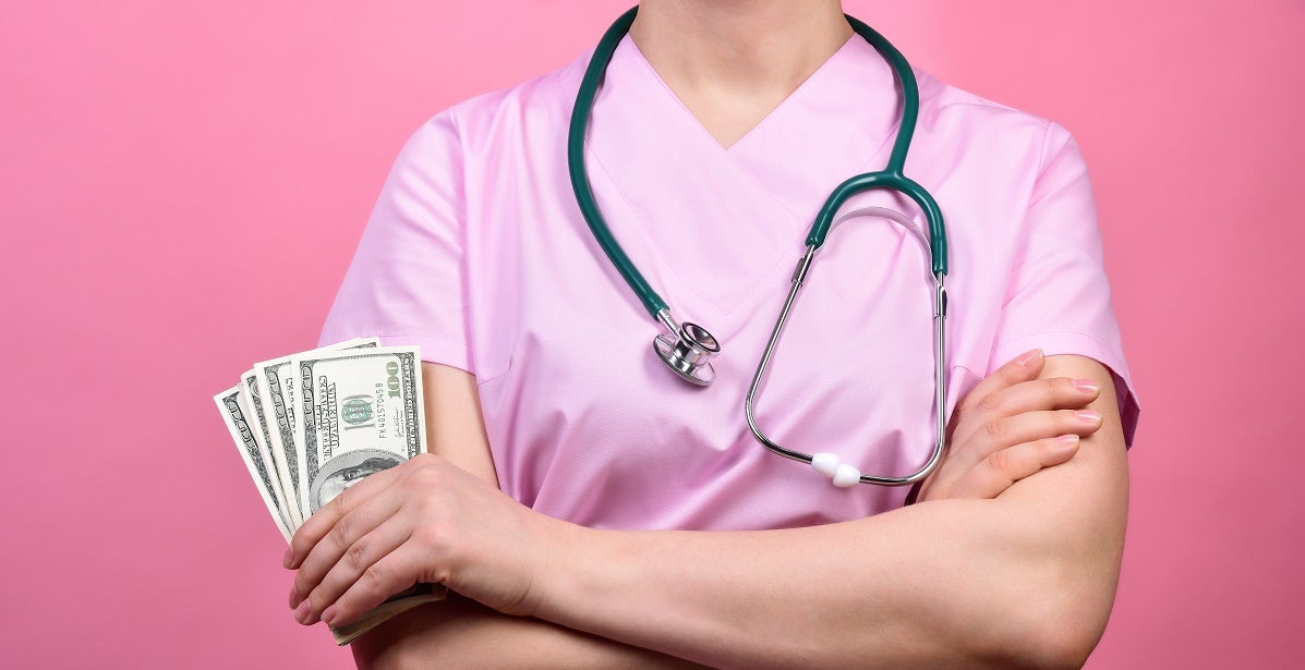 Nurse in a pink medical scrubs holds dollars in her hands.
